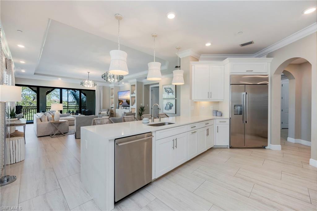 Kitchen featuring arched walkways, stainless steel appliances, white cabinets, open floor plan, and ornamental molding