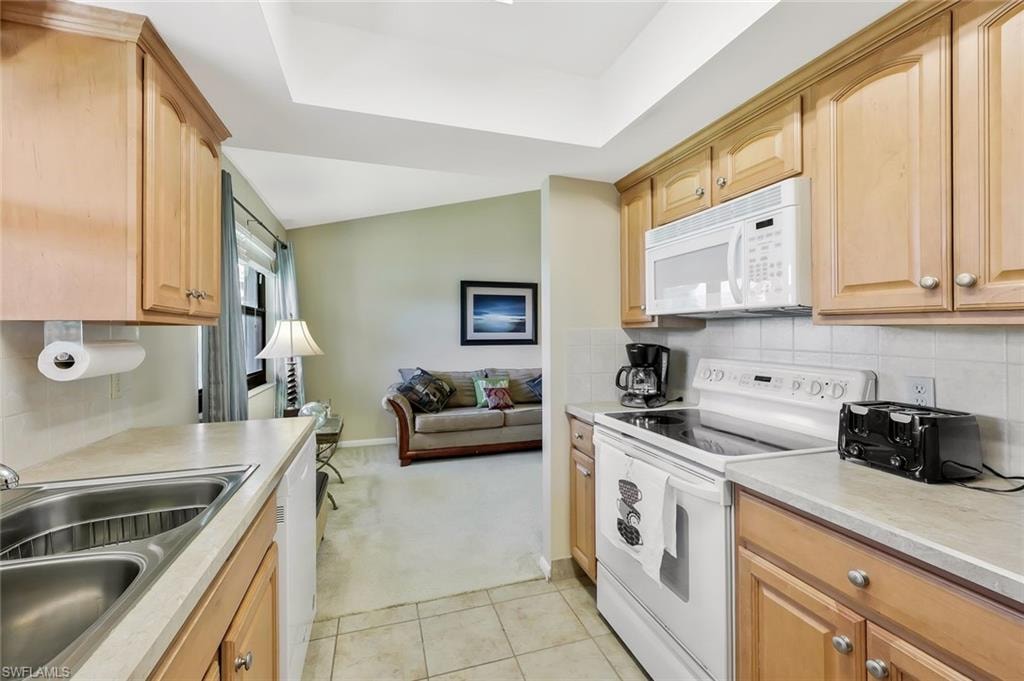 Kitchen with white appliances, light countertops, light carpet, backsplash, and light wood finish cabinetry