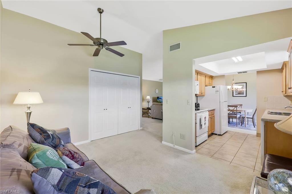 Living area with light carpet, lofted ceiling, light tile patterned floors, a raised ceiling, and ceiling fan