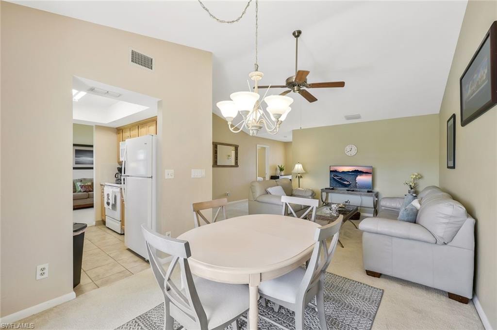 Dining space featuring a chandelier, ceiling fan, light carpet, and lofted ceiling