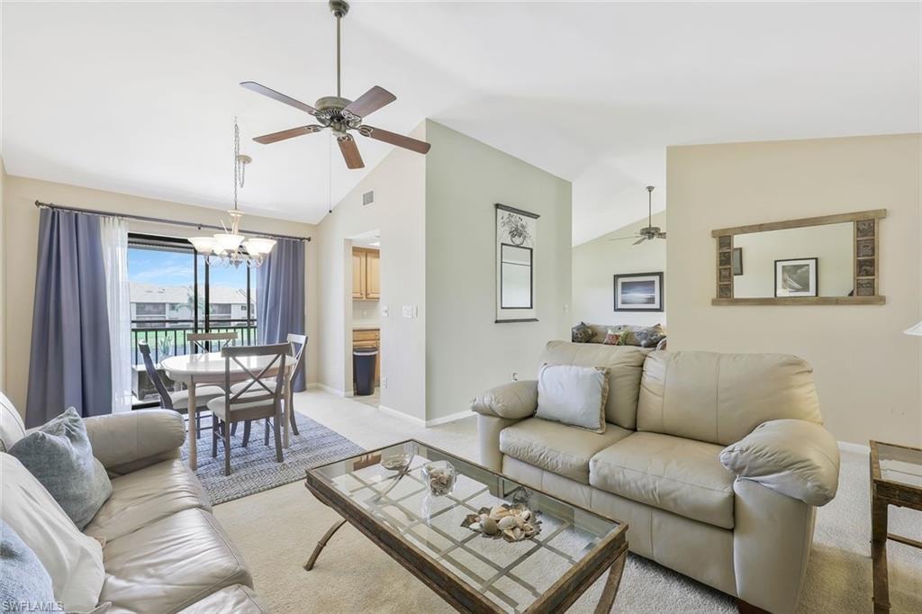 Living room featuring light colored carpet, ceiling fan, a chandelier, and vaulted ceiling