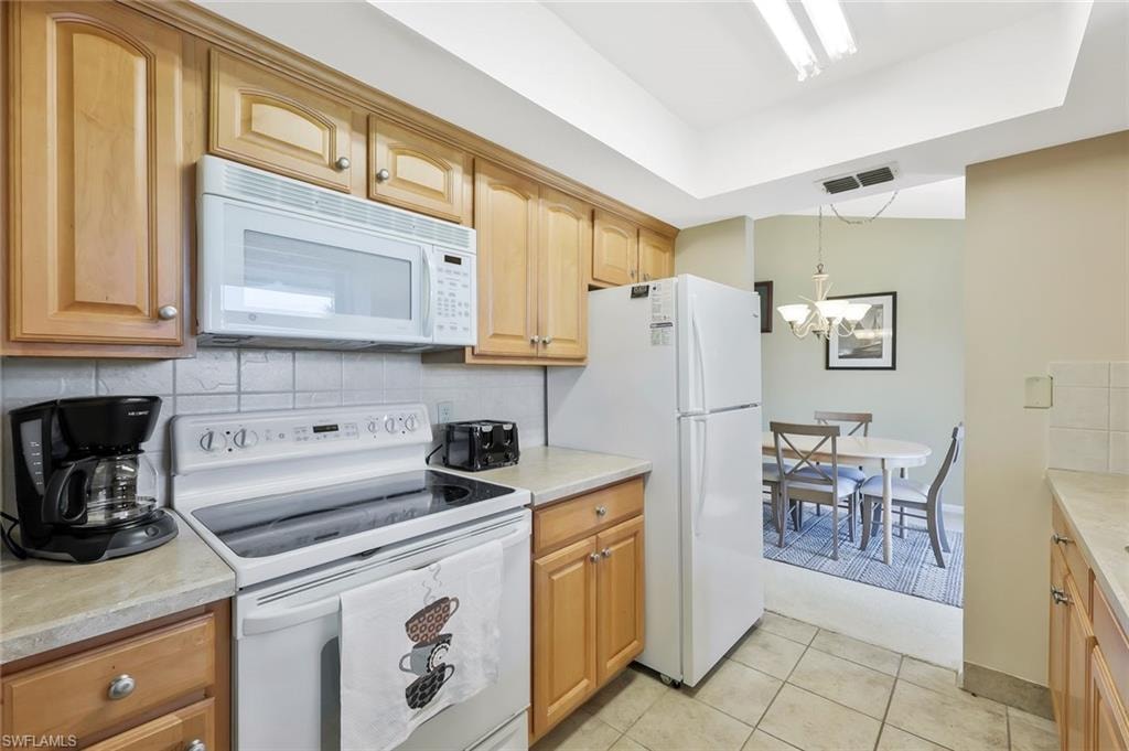 Kitchen with white appliances, light countertops, light tile patterned floors, and tasteful backsplash