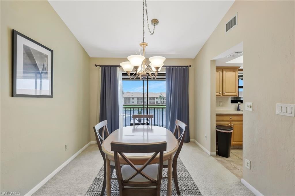 Dining space featuring light colored carpet, a chandelier, and lofted ceiling
