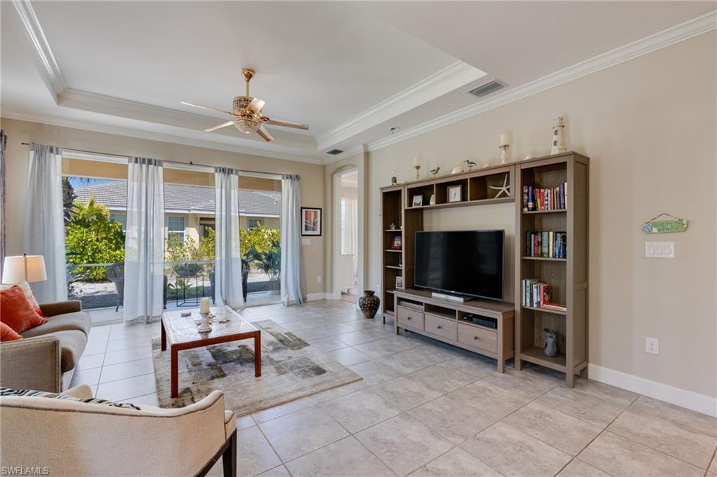 Living room with a ceiling fan, a tray ceiling, and crown molding