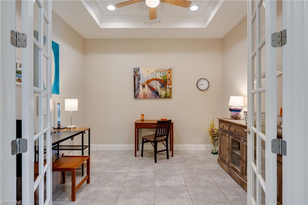 Office space with french doors, ornamental molding, ceiling fan, a raised ceiling, and light tile patterned floors