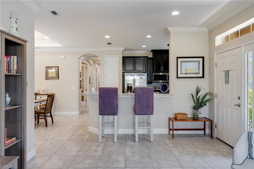 Kitchen featuring arched walkways, dark cabinets, stainless steel appliances, crown molding, and a peninsula