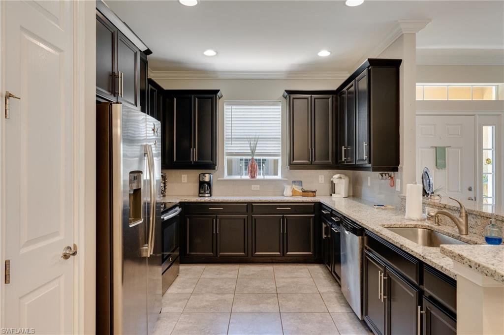 Kitchen with stainless steel appliances, light stone counters, crown molding, light tile patterned flooring, and backsplash