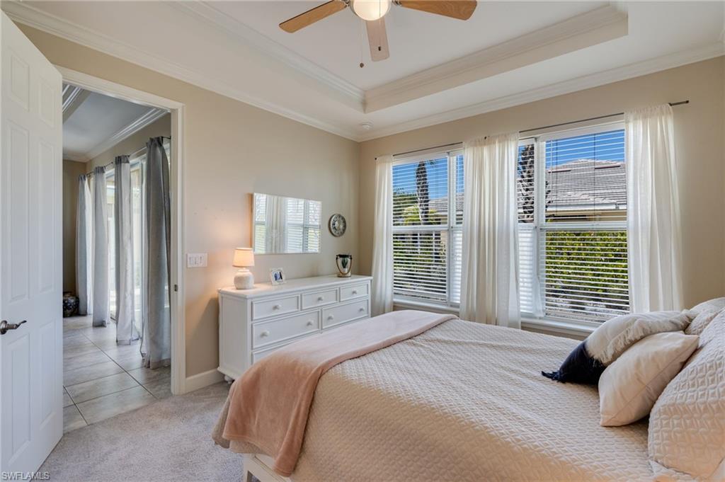 Bedroom with ornamental molding, ceiling fan, multiple windows, light carpet, and a tray ceiling