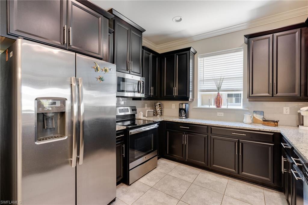 Kitchen featuring stainless steel appliances, light stone countertops, ornamental molding, tasteful backsplash, and light tile patterned floors