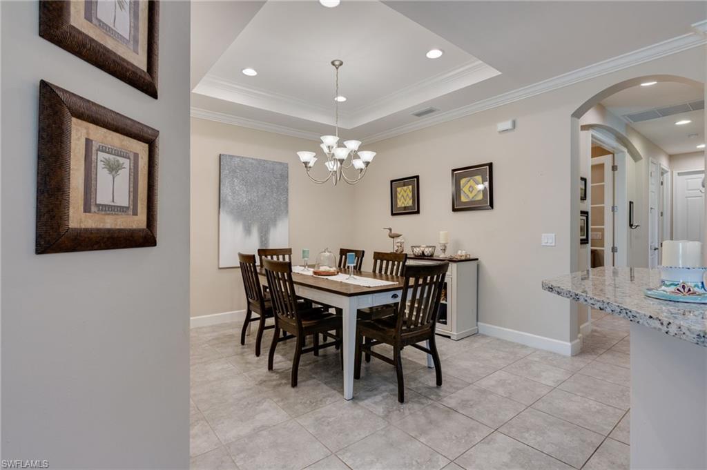 Dining area featuring crown molding, arched walkways, a chandelier, light tile patterned floors, and a raised ceiling