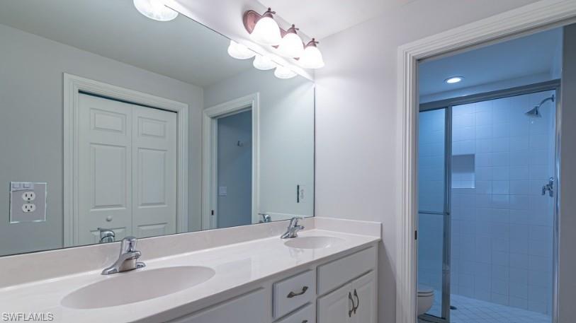 Full bath featuring double vanity, toilet, a tile shower, and a sink
