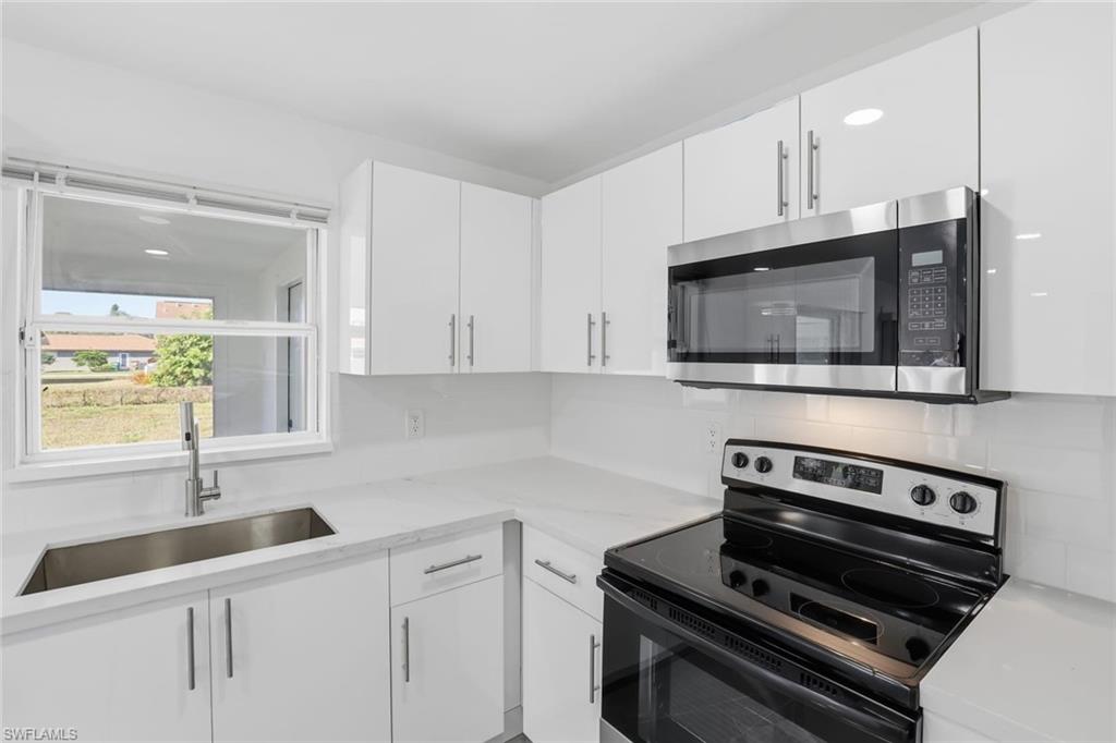 Kitchen with electric stove, stainless steel microwave, white cabinetry, and light stone counters