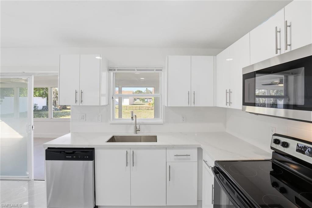 Kitchen featuring stainless steel appliances, light stone countertops, and white cabinetry