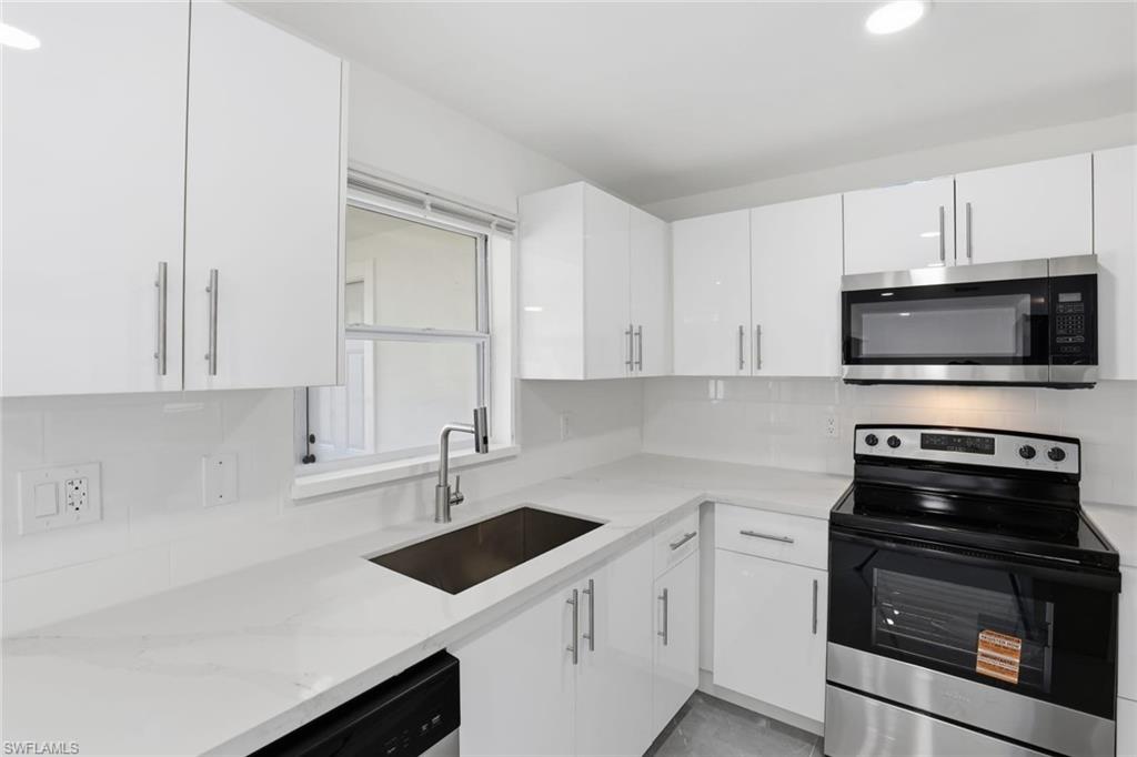 Kitchen featuring stainless steel appliances, backsplash, white cabinetry, light stone counters, and recessed lighting
