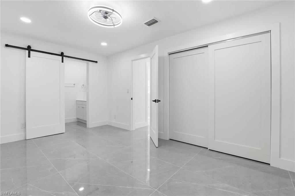 Unfurnished bedroom featuring a barn door, connected bathroom, recessed lighting, and a closet