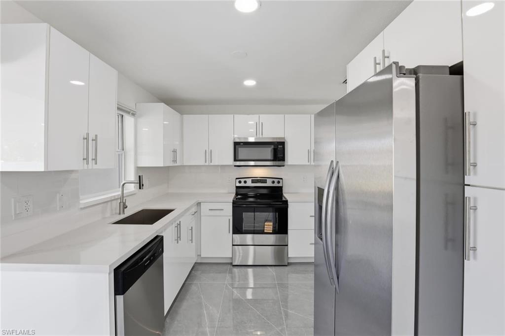 Kitchen featuring stainless steel appliances, white cabinets, recessed lighting, and light stone countertops