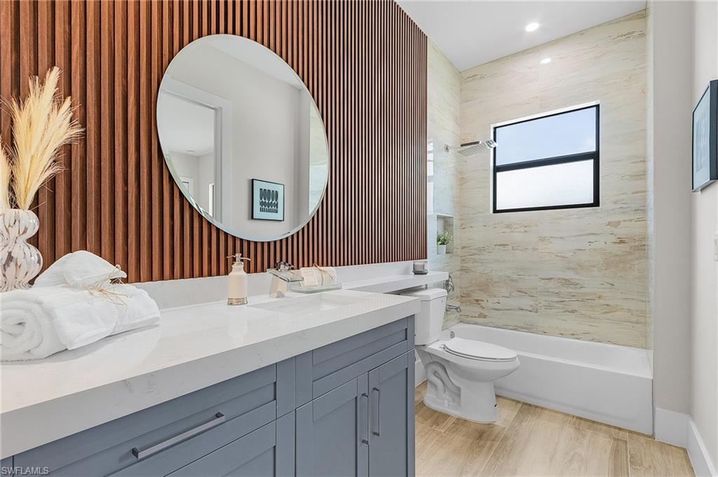 Bathroom with vanity, shower / bathtub combination, light wood finished floors, and wallpapered walls