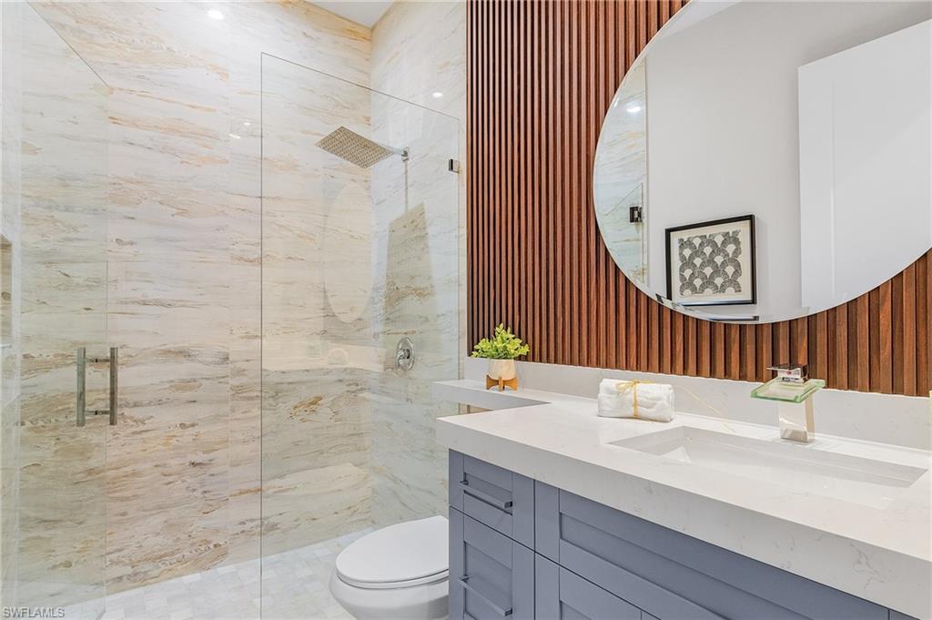 Full bathroom featuring vanity, a marble finish shower, and wallpapered walls