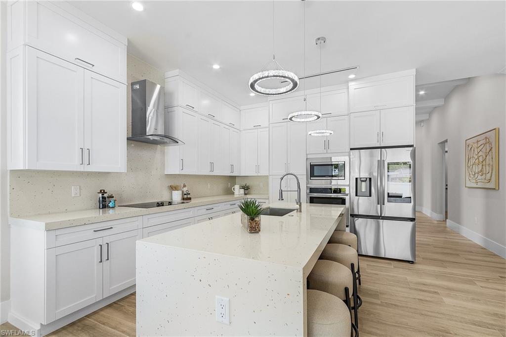 Kitchen with a kitchen bar, stainless steel appliances, light stone counters, and light wood finished floors