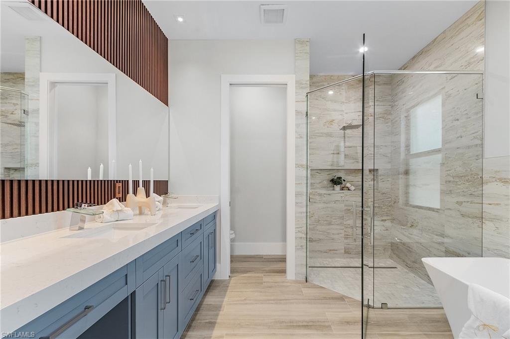 Full bathroom featuring double vanity, a freestanding tub, a marble finish shower, and light wood-type flooring