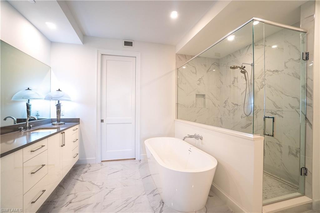 Full bathroom featuring a marble finish shower, light marble finish flooring, a freestanding tub, vanity, and recessed lighting