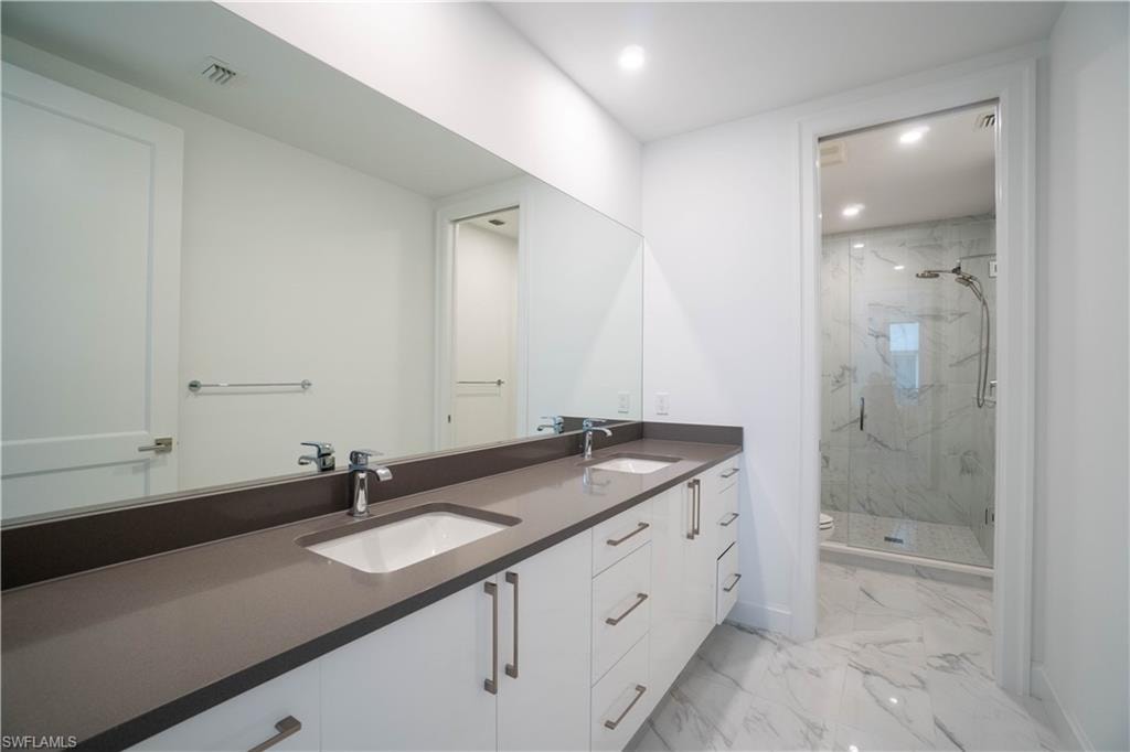 Bathroom with double vanity, a marble finish shower, light marble finish floors, and recessed lighting