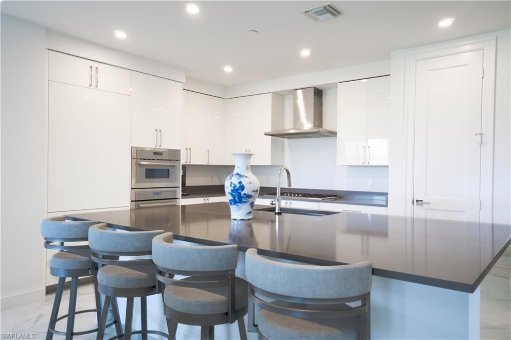 Contemporary kitchen featuring a large central island with seating, high-gloss white cabinetry, stainless steel appliances, and recessed lighting