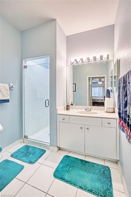 Full bath with vanity, a stall shower, a textured wall, and light tile patterned floors