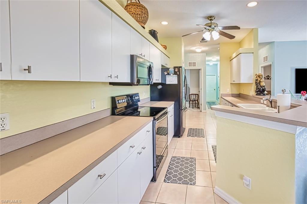 Kitchen with electric stove, a peninsula, stainless steel microwave, white cabinetry, and light countertops