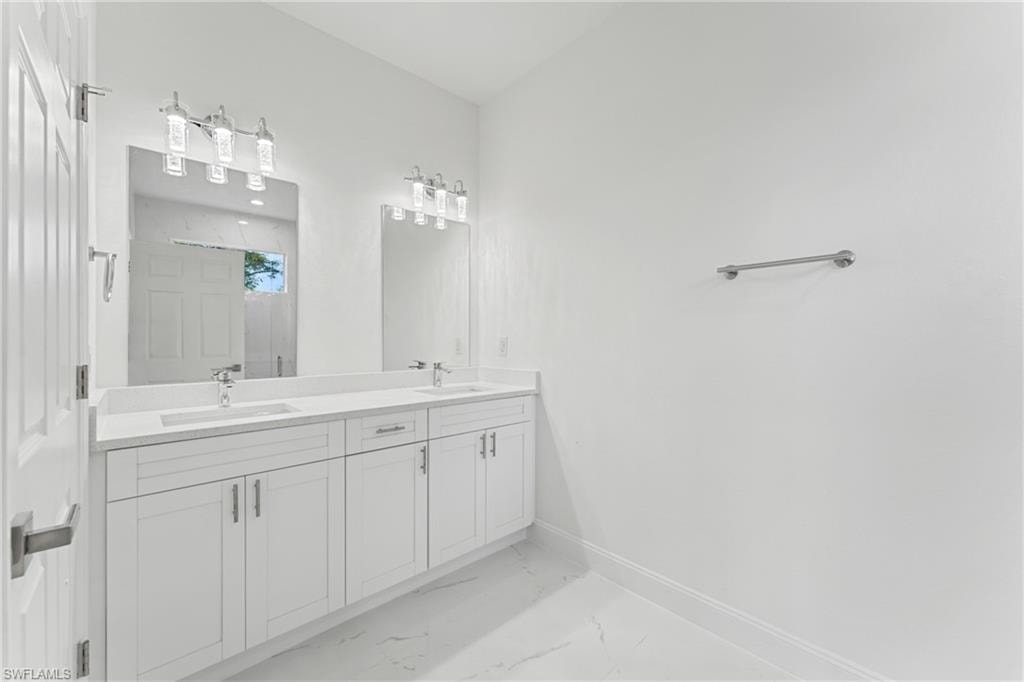 Full bathroom with double vanity, marble finish floor, baseboards, and a sink