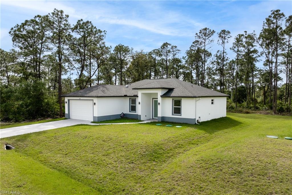 View of front of home with a garage, driveway, a front lawn, and stucco siding