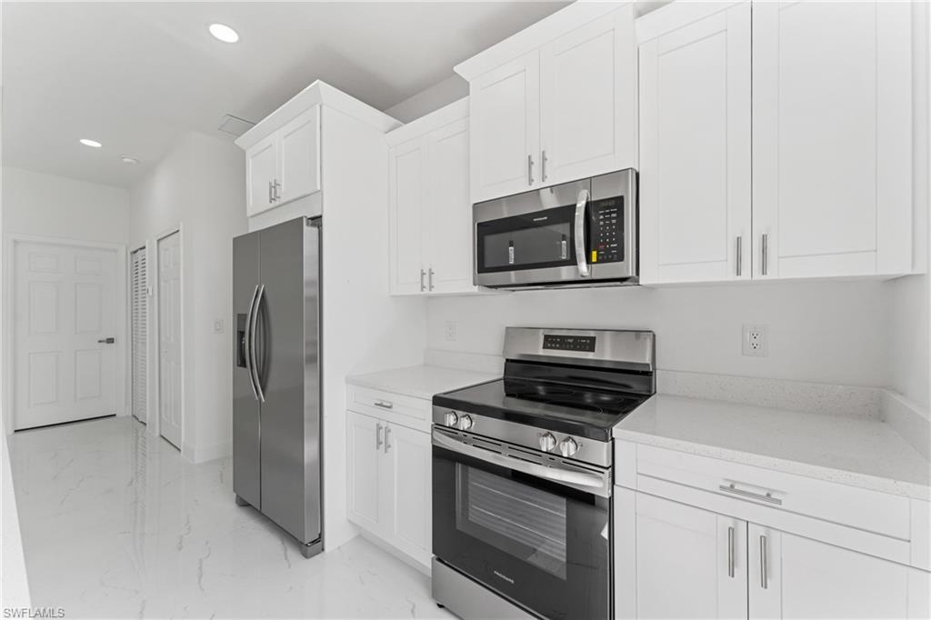 Kitchen with light stone counters, marble finish floor, recessed lighting, appliances with stainless steel finishes, and white cabinets