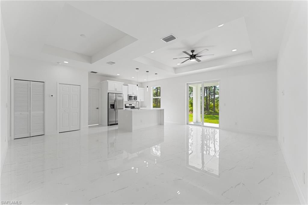Unfurnished living room featuring marble finish floor, a raised ceiling, visible vents, ceiling fan, and baseboards
