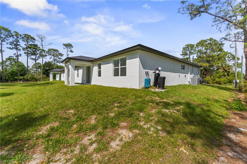 Rear view of property with central air condition unit, a lawn, and stucco siding