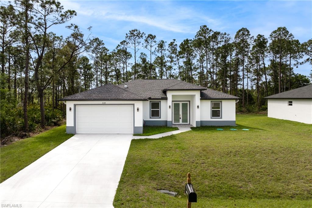 View of front of property featuring an attached garage, driveway, french doors, stucco siding, and a front lawn