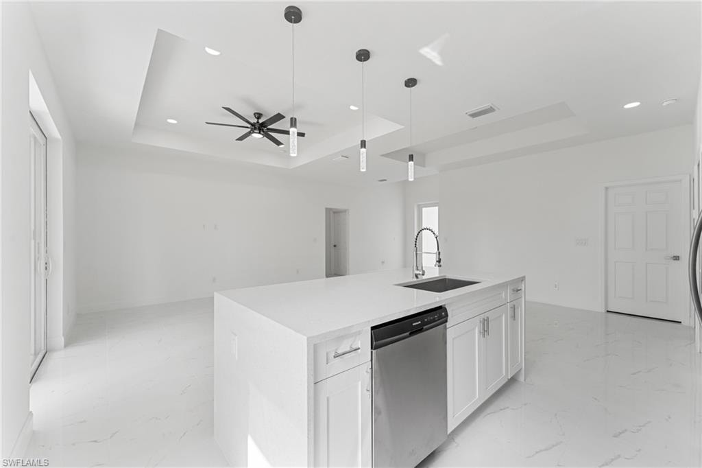 Kitchen with a sink, marble finish floor, a tray ceiling, and dishwasher