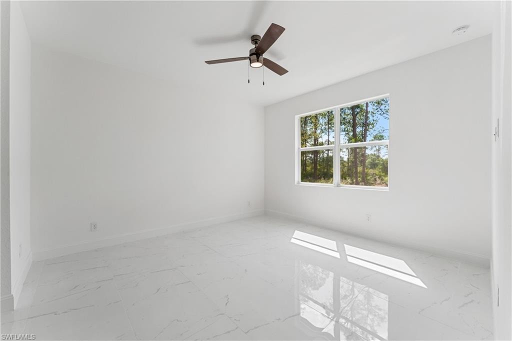 Empty room with marble finish floor, baseboards, and a ceiling fan