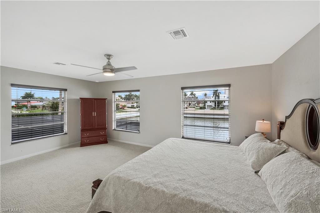 Bedroom featuring light colored carpet, multiple windows, and ceiling fan