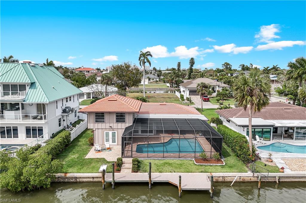 Back of property with a patio, an outdoor pool, a lanai, a water view, and a lawn