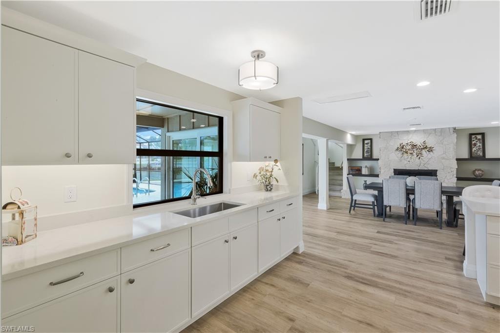 Kitchen featuring white cabinets, light wood-style flooring, decorative light fixtures, light stone counters, and open floor plan