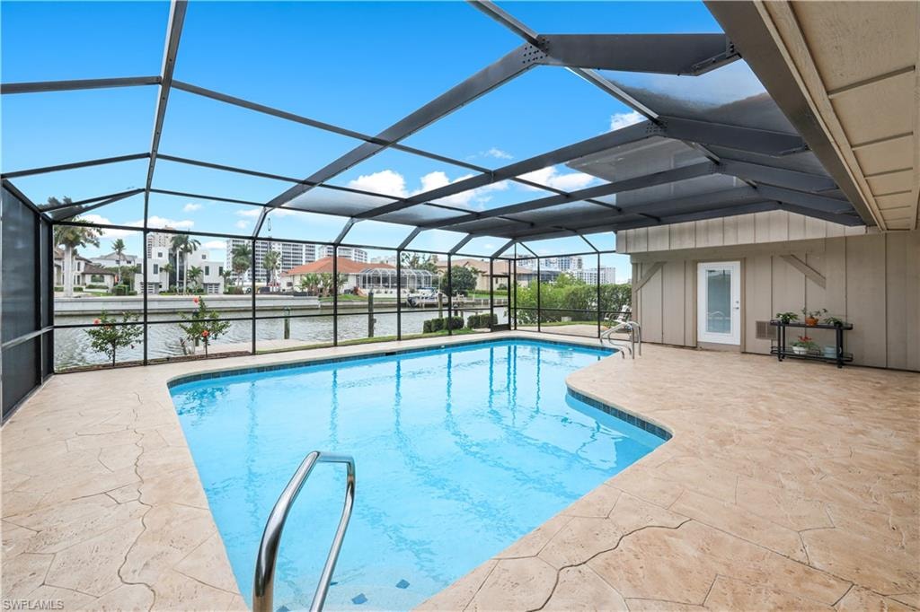 Outdoor pool featuring a sunroom, a patio area, glass enclosure, and a residential view