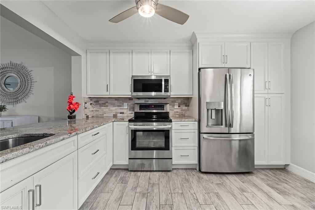 Kitchen with stainless steel appliances, light stone countertops, white cabinetry, and ceiling fan