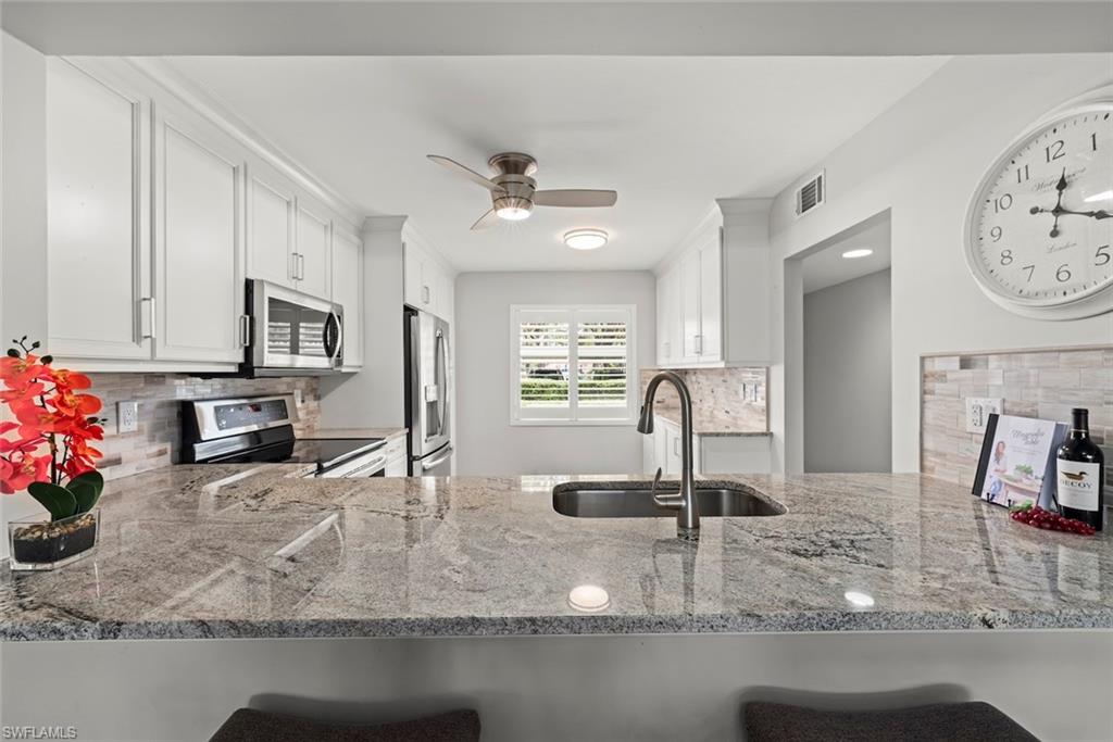 Kitchen featuring backsplash, white cabinets, stainless steel appliances, light stone counters, and a peninsula