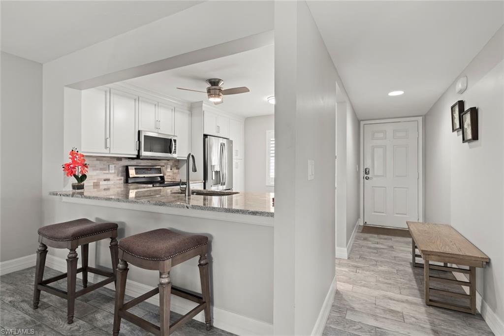 Kitchen with light wood-style floors, light stone counters, white cabinetry, a peninsula, and a breakfast bar