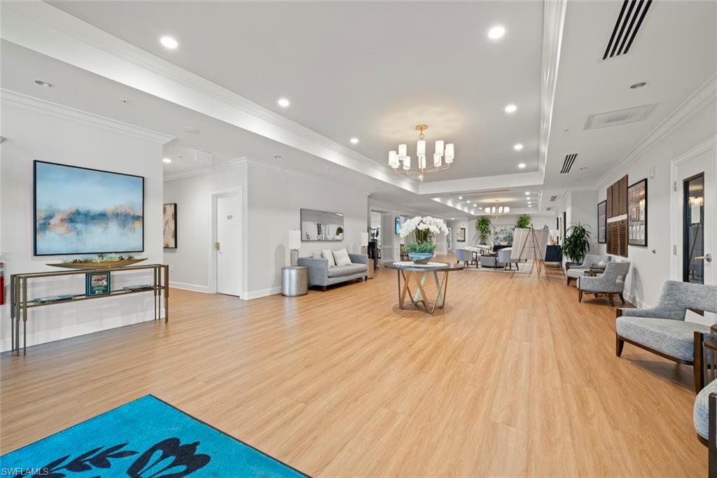 Living area featuring light wood-style floors, crown molding, hanging lights, and a raised ceiling