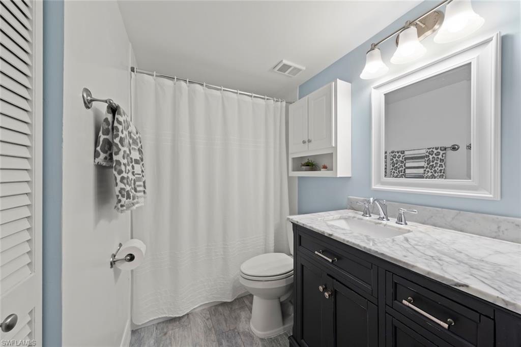 Full bathroom with vanity, dark wood-style floors, a shower with shower curtain, and a closet