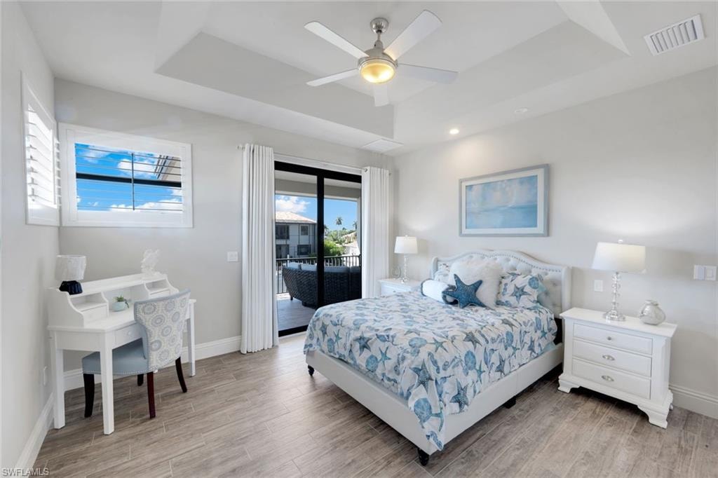 Bedroom featuring a raised ceiling, light wood-style floors, access to exterior, and ceiling fan