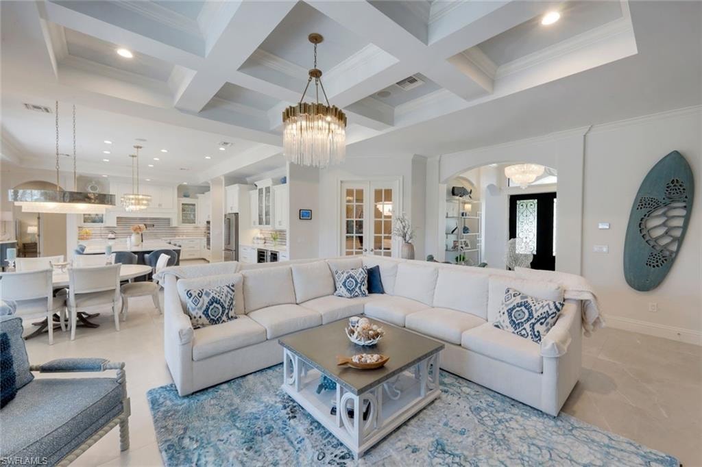Living room featuring hanging lights, ornamental molding, coffered ceiling, and arched walkways