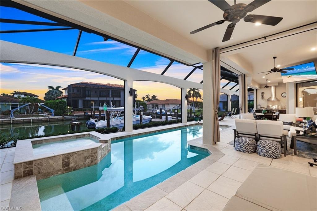 Combined pool / hot tub featuring a patio area, a sunroom, an outdoor living / dining area, glass enclosure, and a water view