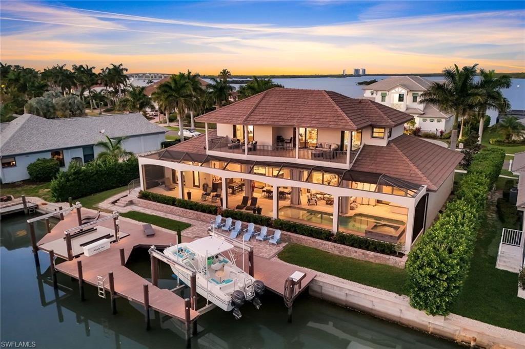 Back of house at dusk featuring a patio area, boat lift, an outdoor pool, a water view, and stucco siding